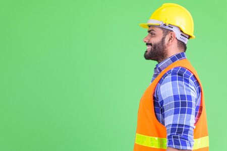 Profile view of happy young overweight bearded Indian man construction worker smilingの写真素材