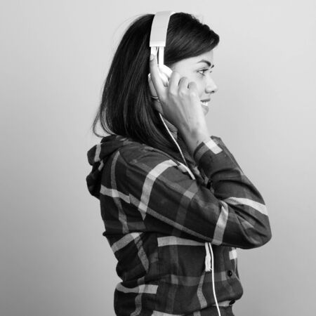 Young beautiful Indian woman listening to music against gray backgroundの写真素材