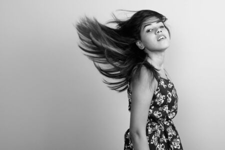 Young beautiful Indian woman wearing dress while flipping hair against gray background
