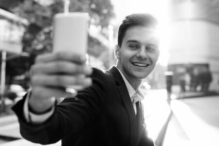 Young handsome businessman using mobile phone in city to take selfieの写真素材
