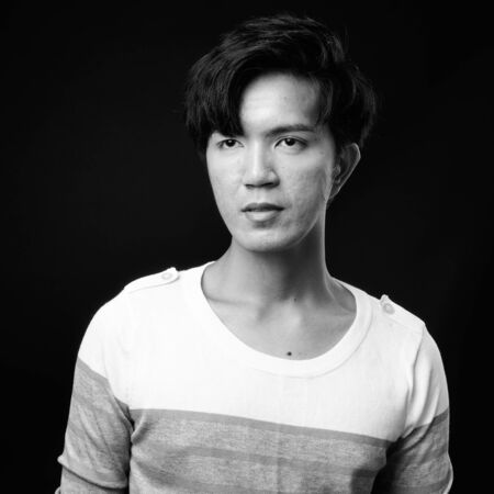 Young handsome Asian man thinking against black backgroundの写真素材