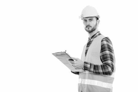 Studio shot of young man construction worker writing on clipboard