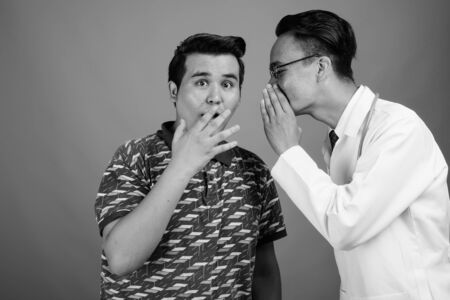 Young multi-ethnic man and young Indian man doctor against gray backgroundの写真素材