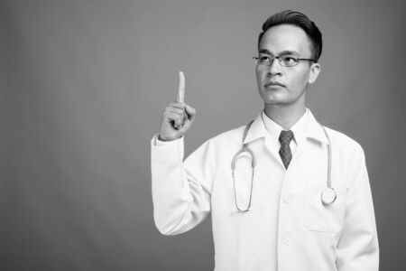 Young handsome Indian man doctor against gray backgroundの写真素材