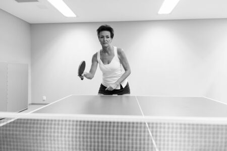 Mature beautiful woman playing table tennis indoorsの写真素材