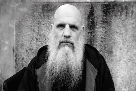 Mature bald man with long gray beard against concrete wall outdoorsの写真素材