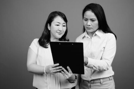 Two mature Asian businesswomen together looking documentsの写真素材