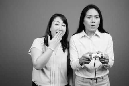 Two mature Asian businesswomen playing video games together
