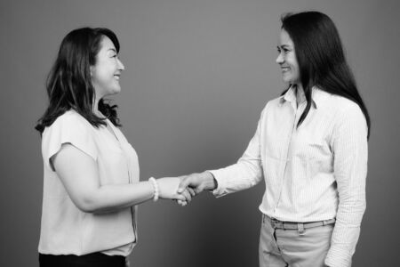 Two mature Asian businesswomen together studio shot in black and white