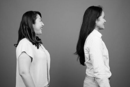 Two mature Asian businesswomen together profile view studio shot in black and whiteの写真素材