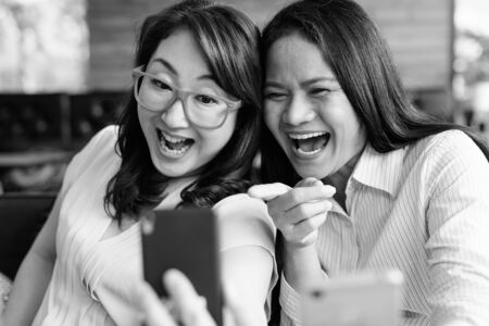 Happy Asian women using mobile phone together while hanging out at the coffee shopの写真素材