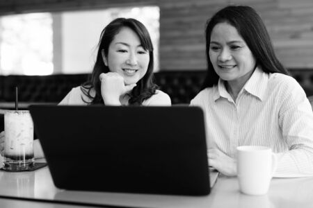 Two mature Asian women using laptop computer at coffee shopの写真素材