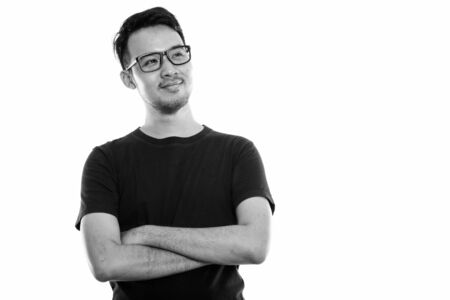 Studio shot of young Asian man thinking while wearing eyeglasses with arms crossed