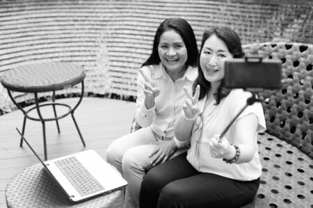 Happy women taking selfie with mobile phone attached to selfie stickの写真素材