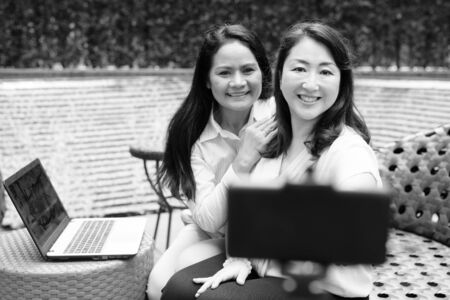 Happy women taking selfie with mobile phone attached to selfie stick