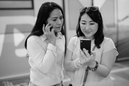 Two mature Asian women together at the train station using mobile phoneの写真素材