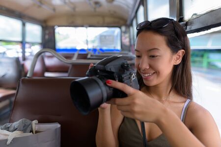 Young tourist woman sitting at bus while using DSLR cameraの写真素材