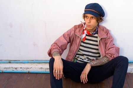 Young handsome rebellious man sitting outdoors while thinking