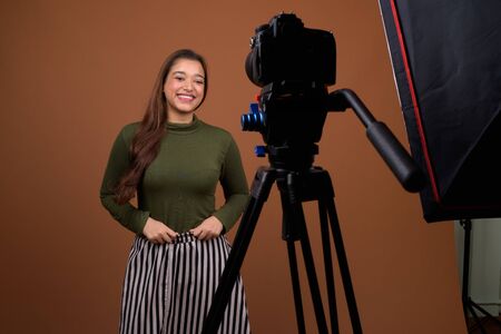 Young beautiful Indian woman vlogging against brown background