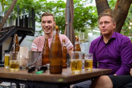 Men talking and laughing while drinking beer outdoors