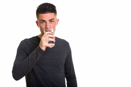 Studio shot of young handsome man drinking glass of water