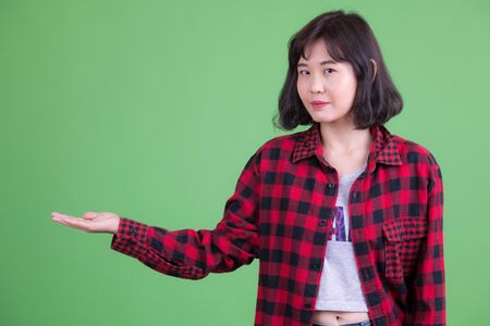 Portrait of beautiful Asian hipster woman showing somethingの写真素材
