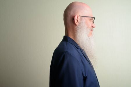 Studio shot of mature bald businessman with long beard wearing suit and eyeglasses against white backgroundの写真素材