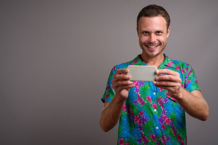 Portrait of handsome tourist man using phone ready for vacation against gray background