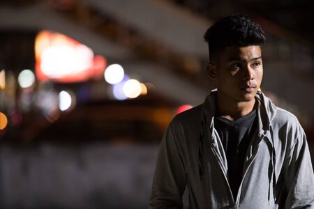 Young Asian man thinking in the city streets at nightの写真素材