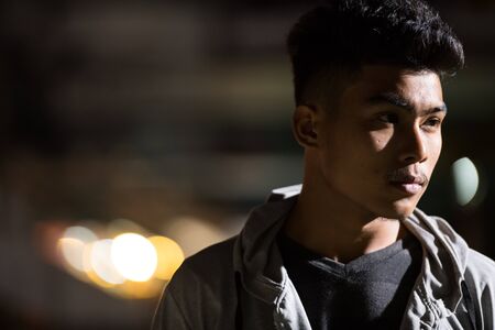 Face of young Asian man thinking in the city streets at nightの写真素材