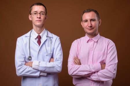 Young man doctor and man patient against brown backgroundの写真素材