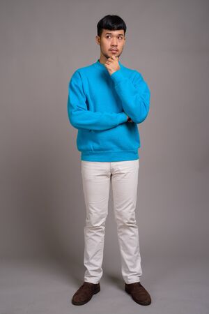 Portrait of young Asian man against gray backgroundの写真素材