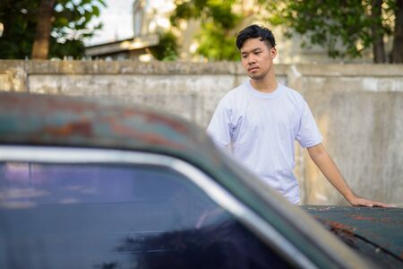 Young Asian man with rusty old car in the streets outdoorsの写真素材