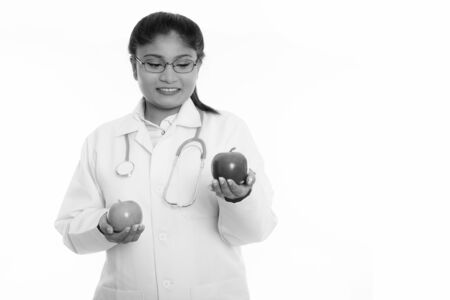 Studio shot of young happy fat Persian woman doctor smiling while holding green apple and looking at red appleの写真素材