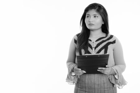 Studio shot of young fat Persian businesswoman thinking while holding clipboardの写真素材