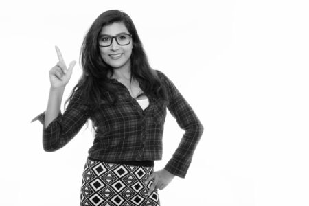Studio shot of young happy Persian woman smiling while pointing finger up with eyeglasses isolatedの写真素材