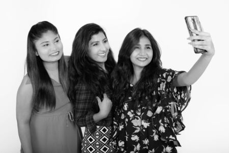 Three happy young Persian woman friends smiling while taking selfie picture with mobile phone togetherの写真素材