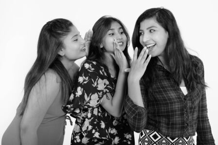 Studio shot of young happy Persian woman looking shocked with both friends whispering on one sideの写真素材