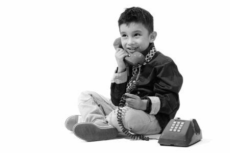 Studio shot of cute happy boy smiling and talking on old telephone while thinkingの写真素材