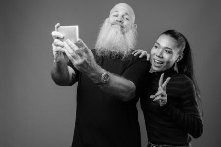 Mature bearded bald man with young Asian transgender woman together in black and whiteの写真素材