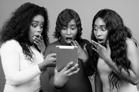 Young beautiful African twin sisters and friend against gray backgroundの写真素材