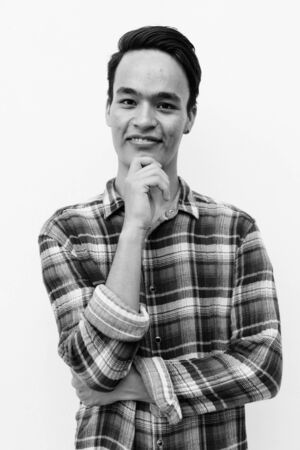 Young handsome Indian man against white wall outdoors in black and whiteの写真素材