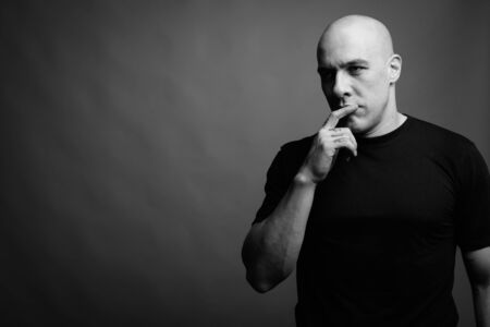 Handsome bald man against gray background in black and whiteの写真素材