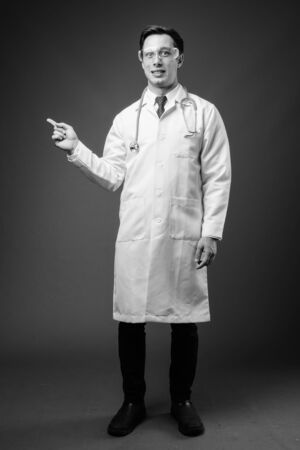 Young handsome man doctor wearing protective glasses in black and whiteの写真素材
