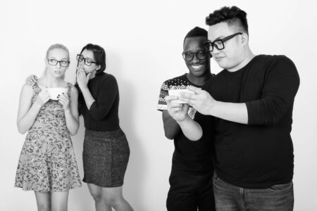 Happy diverse group of multi ethnic friends using mobile phone together with friends having coffee and whispering in the backの写真素材