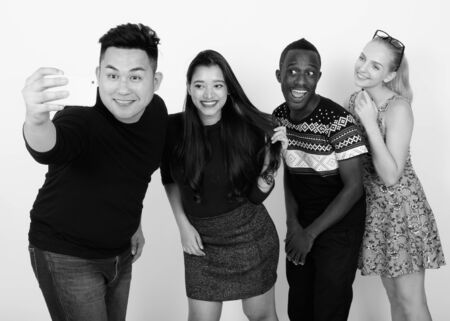 Studio shot of happy diverse group of multi ethnic friends smiling while taking selfie picture with mobile phone togetherの写真素材