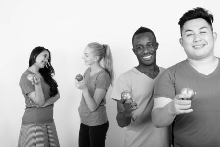 Studio shot of happy diverse group of multi ethnic friends smiling while holding red apple together with friends talking in the backの写真素材