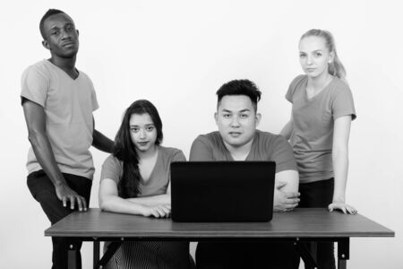 Studio shot of diverse group of multi ethnic friends sitting with laptop on wooden table togetherの写真素材