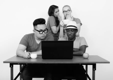 Diverse group of multi ethnic friends using laptop together with friends whispering at the backの写真素材