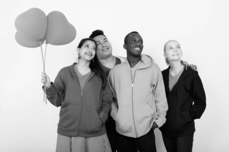 Studio shot of happy diverse group of multi ethnic friends smiling and thinking together while holding bunch of red heart shaped balloonsの写真素材